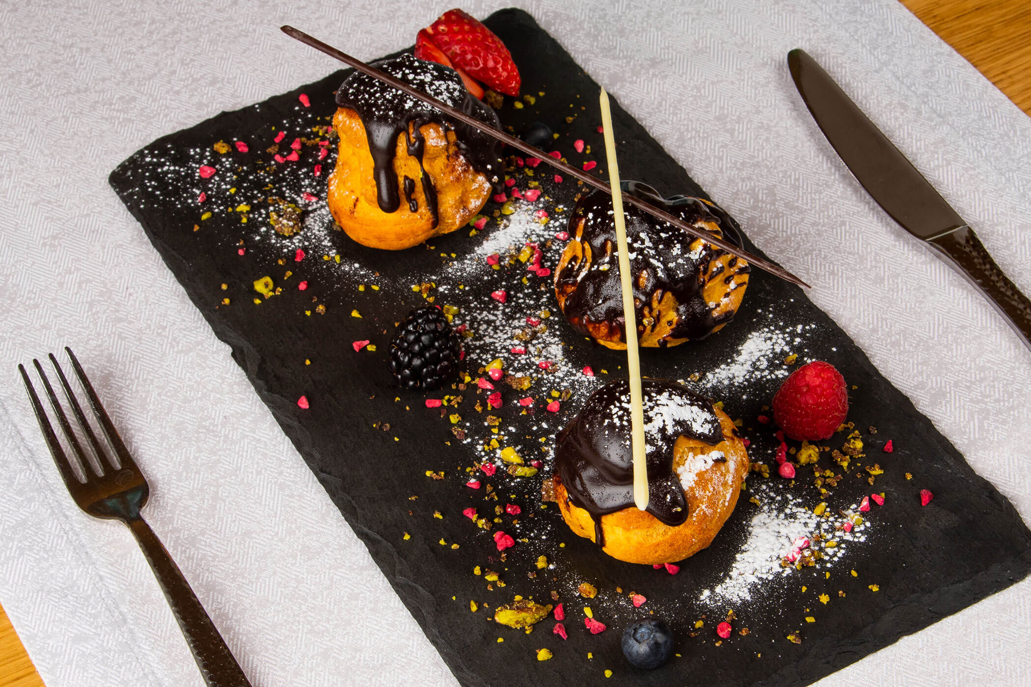 Profiterols mit Früchten auf einer schwarzen Platte - Posta Zirm
