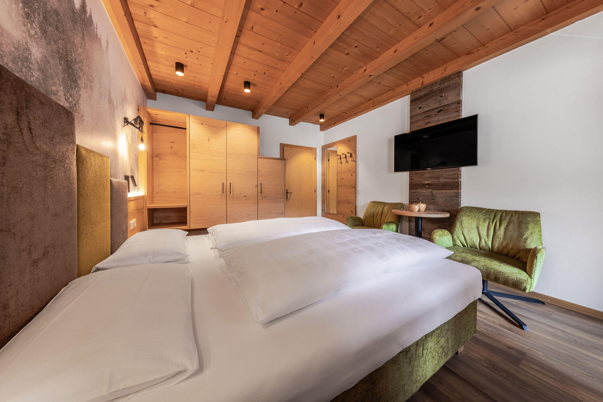 Schlafzimmer mit Sessel, Doppelbett, TV und Schrank in der Ferienwohnung Sassongher - Posta Zirm