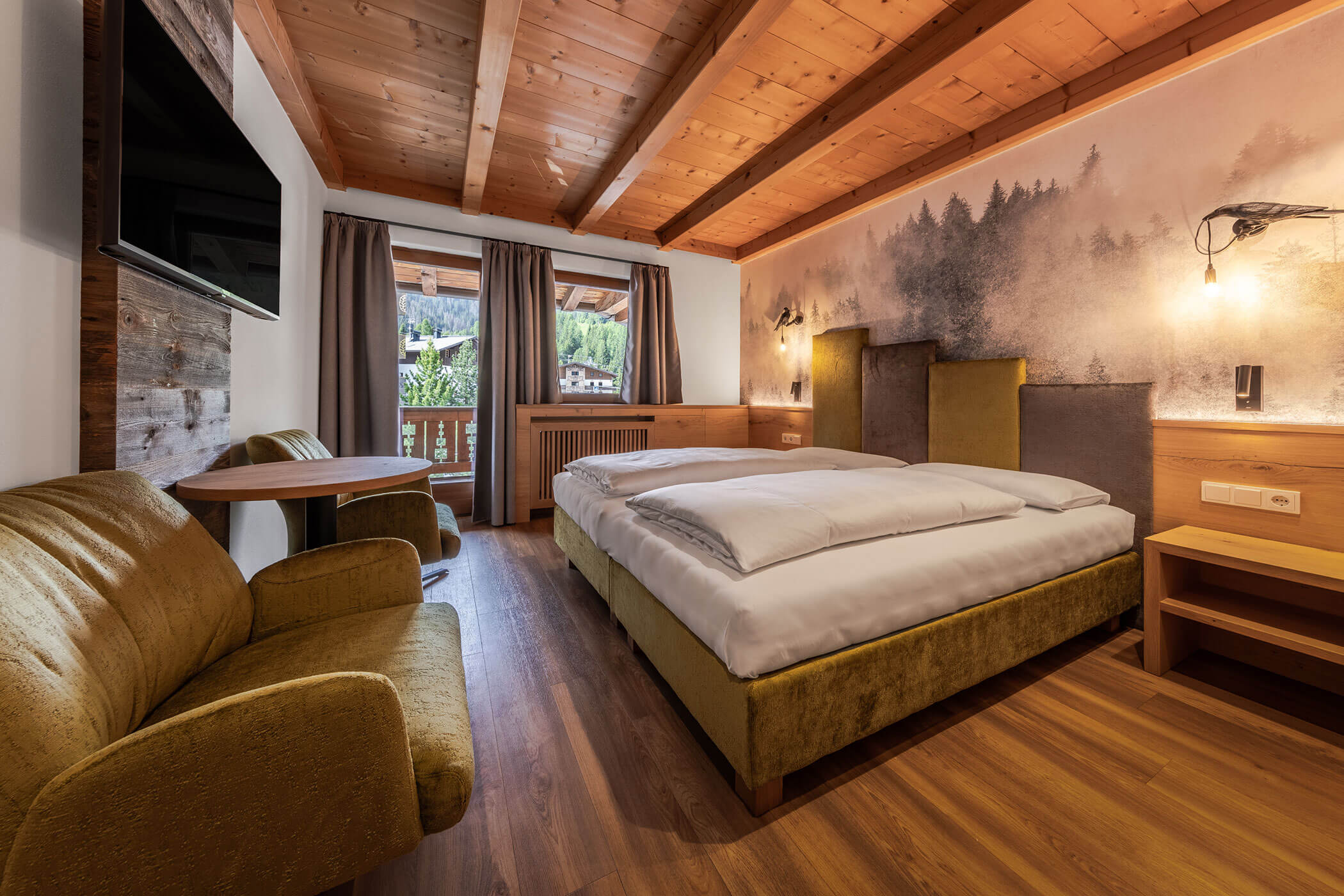 Schlafzimmer mit Doppelbett, zwei Sessel und Blick auf den Balkon in der Ferienwohnung Sassongher - Posta Zirm